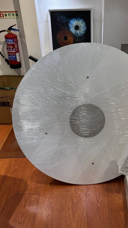 Circular wall-display panel wrapped in protective film, leaning unassembled among boxes