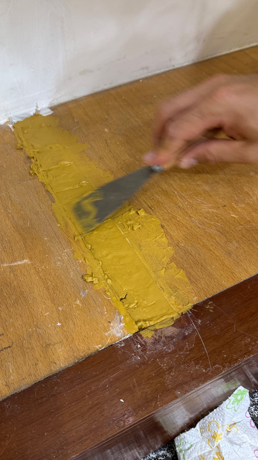 Wood filler being applied to a shelf edge with a putty knife during a touch-up repair